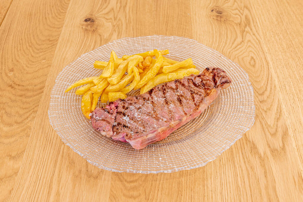 Grilled Galician beef entrecote with fried potatoes on a transparent glass plate - Photo, Image