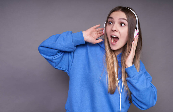 A cheerful, driving, funny, emotional expressive young girl in a blue hoodie and headphones, making grimaces, having fun, experiencing a good mood. - Photo, Image