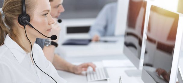 Call center. Group of casual dressed operators at work. Blond business woman in headset at customer service office. Telesales in business - Фото, изображение
