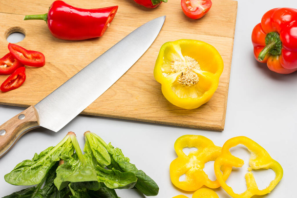 Knife on cutting board, sliced yellow pepper. Spinach leaves. Gray background. Top view - Foto, imagen