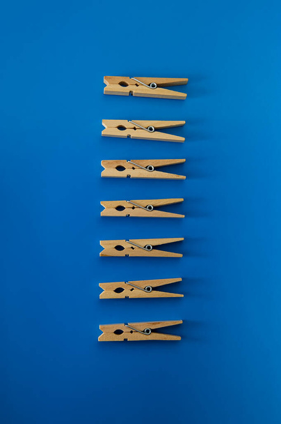 Conceptual composition, seven wooden clothespins arranged in parallel and vertically on a blue background. Cover. - Foto, Imagem