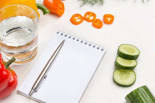 Pepper and sliced cucumber. Pen and notebook. White background. Top view - Foto, imagen