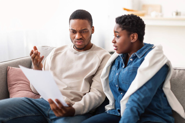 Confused black couple reading documentation at home, sitting on couch - Photo, Image