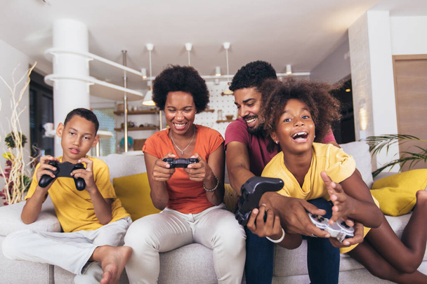 Афроамериканская семья играет в видеоигры вместе и весело проводит время дома - Фото, изображение