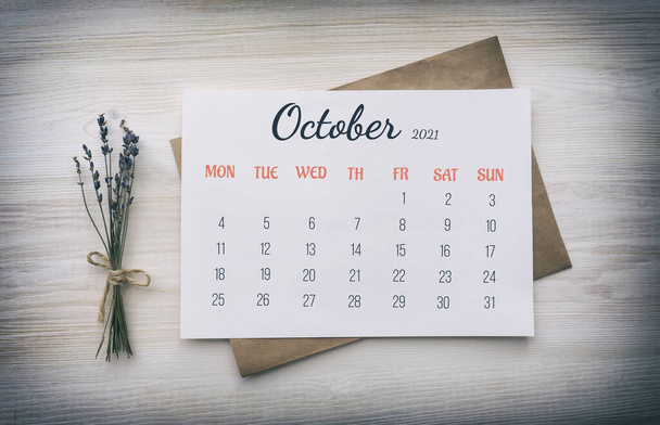 Full-month calendar: October 2021. Numbers, days of week, on white paper, on top of kraft paper envelope, next to bouquet of dried lavender on wooden white background - Zdjęcie, obraz