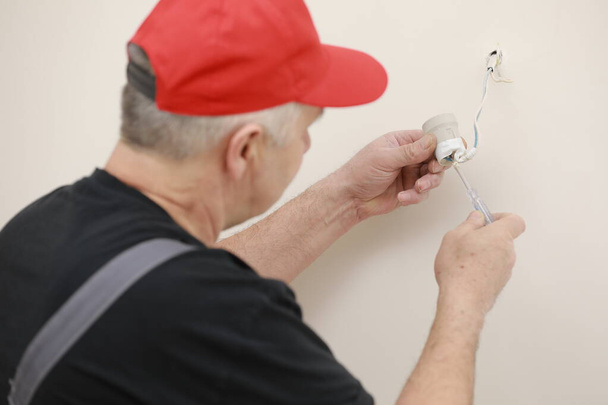 Manos masculinas de electricista instalando zócalo para bombilla. - Foto, imagen