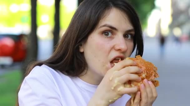 Una donna ghiotta mangia un hamburger di nascosto. Violazione della dieta, guasto sulla strada vicino alla strada. - Filmati, video