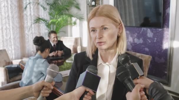 Waist-up shot of successful business woman being interviewed by journalists speaking in microphones during press conference with multi-ethnic partners and investors - Imágenes, Vídeo