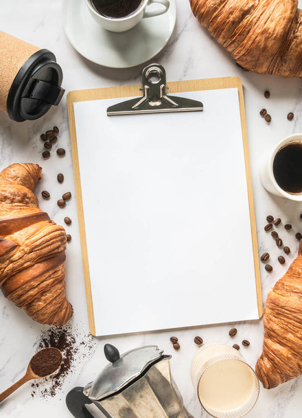 Flat lay frame of cups of coffee, croissants and clipboard with blank sheet for menu entry on marble background. French breakfast concept. Top view. Copy space - Foto, afbeelding