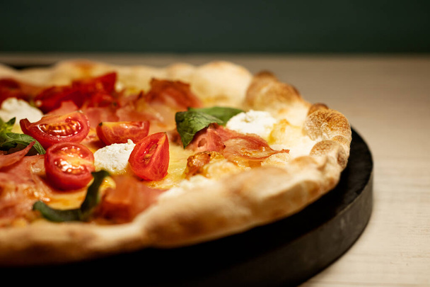 Pizza s rajčatovou zeleninou na černé dřevěné desce rozpůlená v restauraci - Fotografie, Obrázek