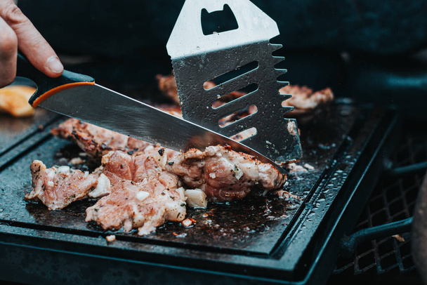 Man slices a pork neck, fragrant and richly seasoned with basil, pepper, salt and other herbs, which is fried on a granite slab over an open fire. Food preparation at a family event. Barbecue season. - Fotoğraf, Görsel