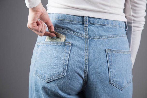 γυναίκα βγάζει χρήματα από την τσέπη σε γκρι φόντο - Φωτογραφία, εικόνα