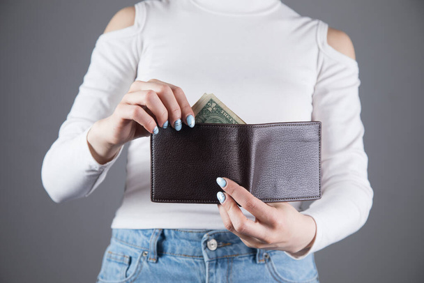 young woman pulls out money from wallet on gray background - Zdjęcie, obraz