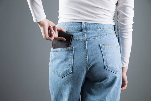 νεαρή γυναίκα βγάζει το πορτοφόλι της από την τσέπη της σε γκρι φόντο - Φωτογραφία, εικόνα