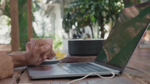 Steadicam de mãos de pessoa irreconhecível digitando no teclado do computador portátil com monitor de tela verde, sentado à mesa com xícara de café ao ar livre - Filmagem, Vídeo