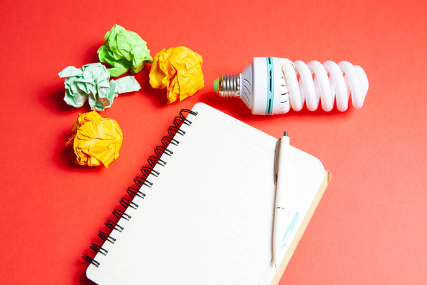 light bulb, notepad and wads of papers on red background - Photo, Image