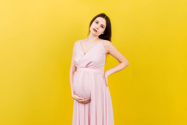 Pregnant woman with a pain in her back on colored Background isolated. - Foto, afbeelding