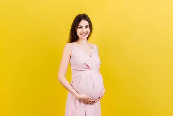 Happy pregnant woman touching her abdomen at Colored background. Future mother is wearing white underwear. Expecting of a baby. Copy space. - Foto, immagini