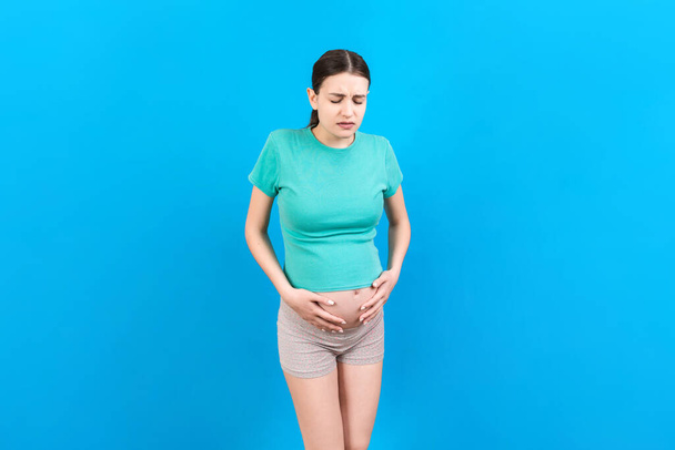 a pregnant girl who has a stomach ache stands on a colored background. isolated. - Φωτογραφία, εικόνα