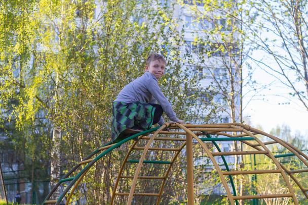A preschool boy climbs metal ladders on a playground in the spring. - Фото, изображение