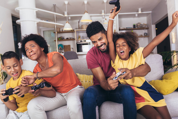 Αφρο-αμερικανική οικογένεια παίζουν βιντεοπαιχνίδια μαζί και διασκεδάζουν στο σπίτι - Φωτογραφία, εικόνα