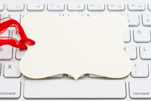 Prázdná dárková značka s červenou stuhou na šedé klávesnici s kopírovacím prostorem pro vaši online prodejní zprávu - Fotografie, Obrázek