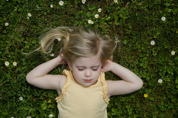 Portret dziewczynki z długimi blond włosami leżącej na zielonej łące - Zdjęcie, obraz