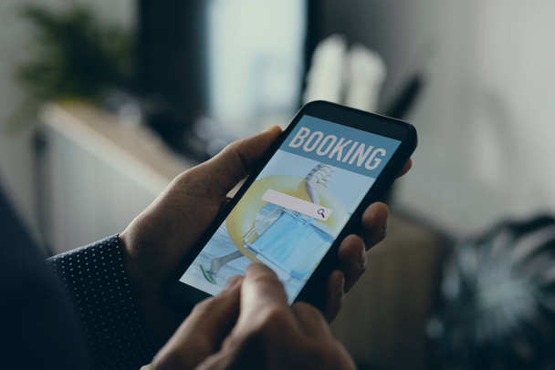 молодий кавказький чоловік, у своїй вітальні, забронював свою відпустку онлайн зі смартфоном, з симульованою пошуковою системою на екрані
 - Фото, зображення