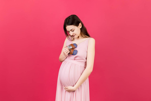 Happy pregnant woman showing small boots for a baby boy at Colored background. Future mother is waiting for a child. Copy space. - Photo, Image