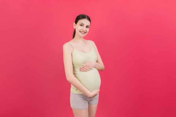 Gelukkig zwangere vrouw aanraken van haar buik op gekleurde achtergrond. Toekomstige moeder draagt wit ondergoed. Verwacht van een baby. Kopieerruimte. - Foto, afbeelding