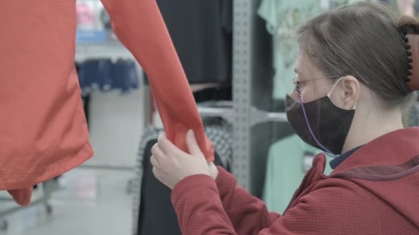 Valkoihoinen nainen naamio virusta vastaan valitsee punainen tuulitakki ostaa varastossa - Materiaali, video