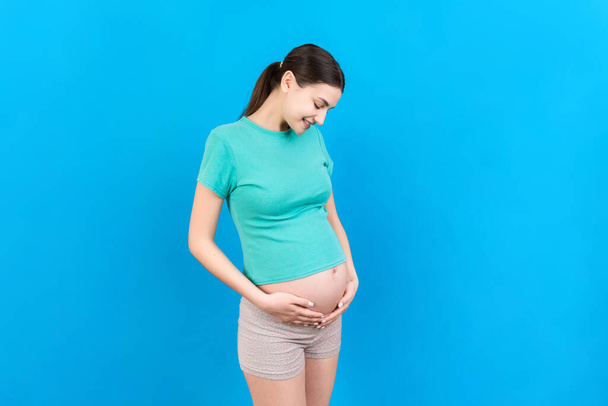 Happy pregnant woman touching her abdomen at Colored background. Future mother. Expecting of a baby. Copy space. - 写真・画像