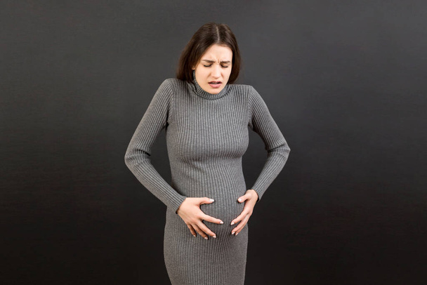 těhotná dívka, která trpí bolestí břicha, stojí na barevném pozadí. izolované. - Fotografie, Obrázek