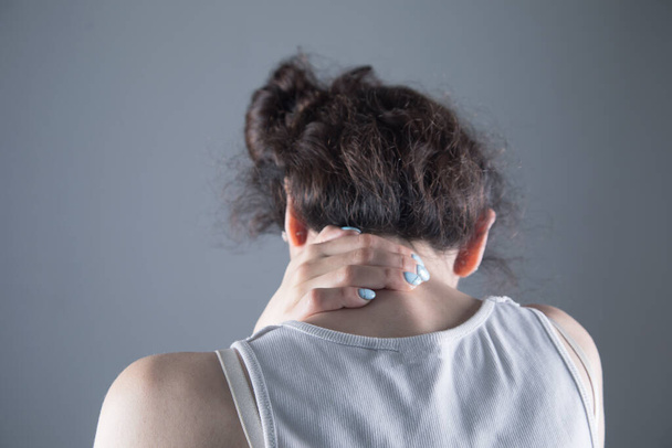 in a young woman, the back of her head hurts on a gray background - Foto, Bild