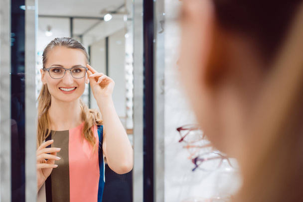 Young woman trying fashionable glasses in optometrist store - Foto, imagen