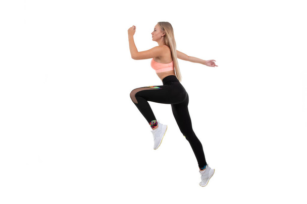 Una joven deportista con un top rosa, polainas y zapatillas de deporte hace ejercicios sobre un fondo blanco - Foto, Imagen