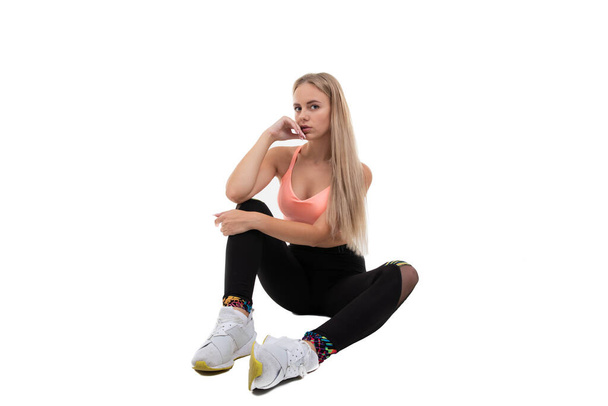 A sporty young woman in a pink top, leggings and sneakers does exercises on a white background - Fotografie, Obrázek
