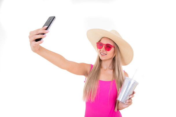 Porträt einer jungen Frau in rosa Badeanzug und Hut, die ein Limonadenglas hält und ein Selfie macht - Foto, Bild