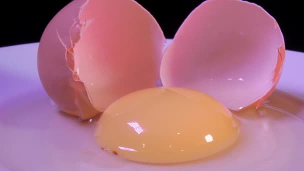 Ένα σπασμένο ωμό αυγό κοτόπουλου με κοχύλια σε ένα πιάτο. Περιστρεφόμενο βίντεο. - Πλάνα, βίντεο