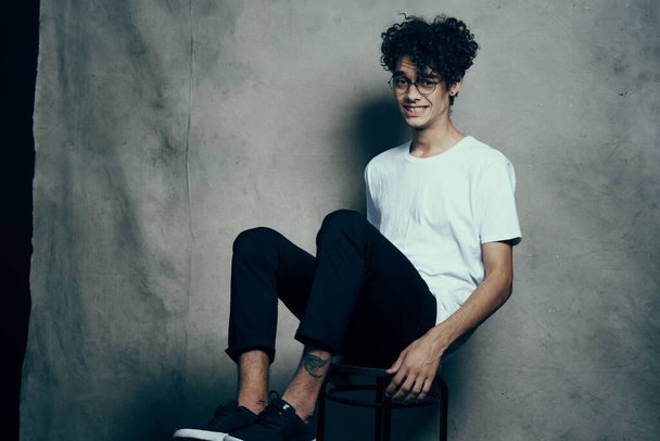 curly-haired guy sitting on a chair with glasses fashion studio - Photo, Image