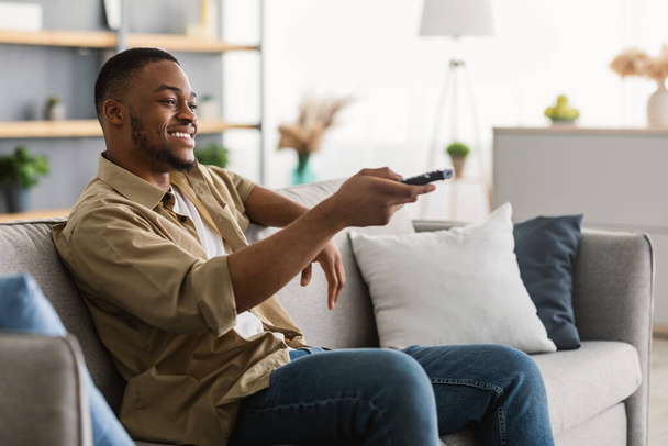 幸せなアフリカ系アメリカ人男性家庭でテレビを見てチャンネルを切り替える - 写真・画像