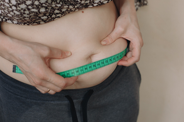 Gruba kobieta mierzy twój tłusty brzuch na jasnym tle - Zdjęcie, obraz