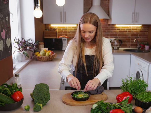 A young blonde happy lady standing in the kitchen while cooking healthy food. Healthy Lifestyle Concept. Cooking at home. decorating and serving the finished dish - Valokuva, kuva