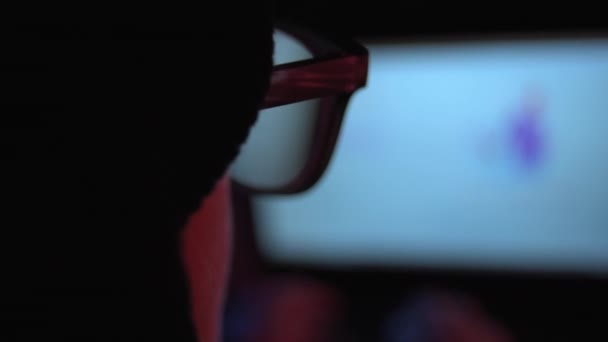 Una estrecha mano sobre la vista del hombro de una hacker usando un ordenador portátil en una habitación oscura - Metraje, vídeo