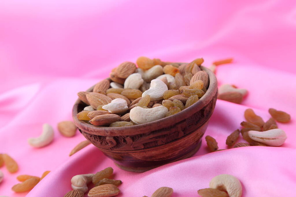 Смачні та здорові змішані сухофрукти, горіхи та насіння в дерев'яній мисці на рожевому шовковому фоні
. - Фото, зображення