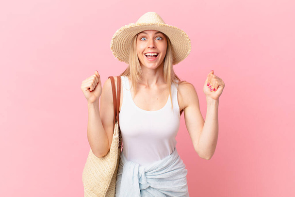 young blonde woman feeling shocked,laughing and celebrating success. summer concept - Фото, изображение