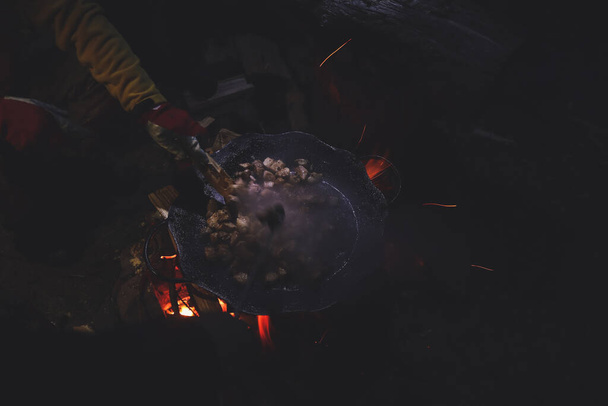 Οι άνθρωποι μαγειρεύουν φαγητό, κρέας στα βουνά σε ένα τηγάνι στη φωτιά. Τουρίστες τη νύχτα. - Φωτογραφία, εικόνα