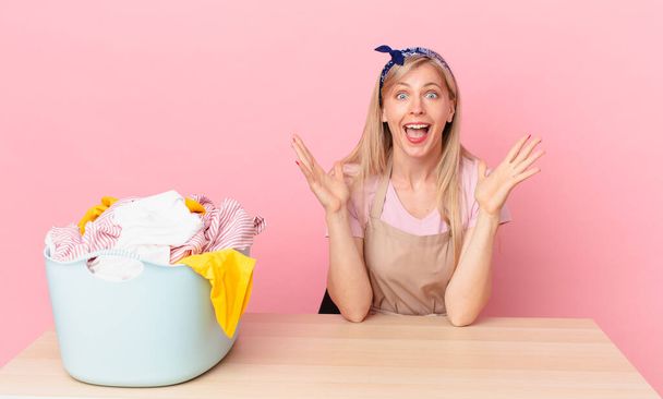 young blonde woman feeling happy and astonished at something unbelievable. wash clothes concept - Foto, Bild