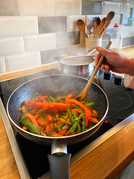 cook's hand in shot preparing a vegan stir fry - speedy vegetable stirfy with tofu - Photo, Image