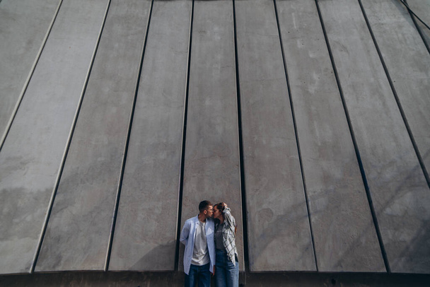 photo of the young couple in love standing near a high wall and kissing - Фото, изображение